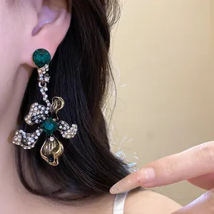 Close-up of vintage floral drop earring featuring green gemstones and sparkling diamonds
