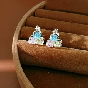 Macro view of geometric earrings featuring blue, pink, and green glass crystals on silver