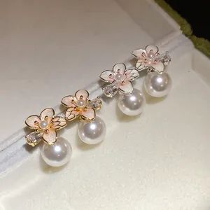 Dettaglio di orecchini a fiore in smalto con perle e zirconi placcati in oro