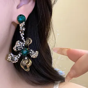 Detailed close-up view of vintage style emerald green rhinestone flower drop earrings on model