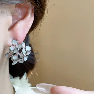 Close-up detail showing elegant floral enamel stud earrings with a pearlescent finish
