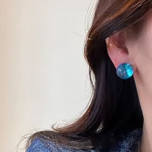 Close-up view of a blue round resin stud earring worn on a model's ear.