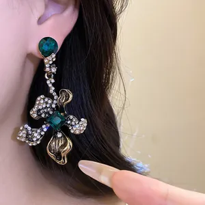 Close-up of vintage floral drop earring with green gems and rhinestones on ear.
