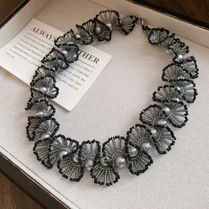 Close-up of elegant handmade grey pearl and black bead woven lace necklace in a jewelry tray