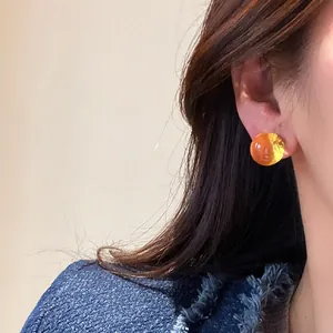 Amber round resin stud earrings shown on model's ear for elegant style.