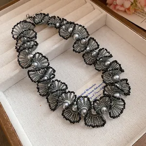 Close-up view of a handcrafted beaded lace necklace with gray pearls and black accents in a box.