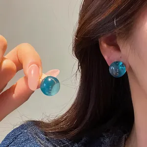 Detailed view of translucent teal round resin stud earrings worn by an Asian model