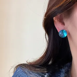 Close-up shot of a minimalist blue resin round stud earring with silver needle worn on ear