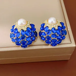 Boucles d'oreilles vintage en or avec pierres bleues et perle sur une boîte à bijoux.