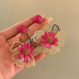 Hand-held view of vibrant magenta raffia flower drop earrings with gold hollow petals.