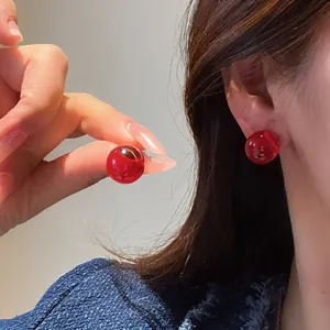 Macro view of elegant red resin ball stud earrings showcasing glossy texture and wear detail.