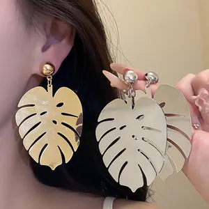 Primo piano di orecchini a pendente a forma di foglia di monstera in oro e argento.
