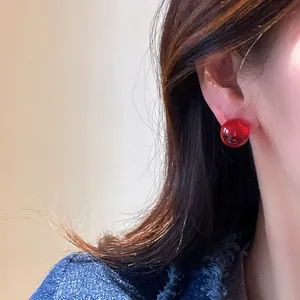 Vibrant red round resin stud earrings worn by a female model in a minimalist style.