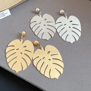 Dettaglio di orecchini a pendente a foglia di monstera oro e argento su sfondo grigio