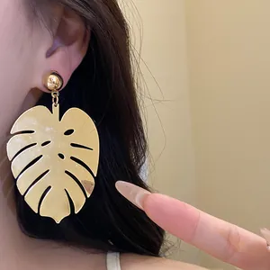 Dettaglio macro di un grande orecchino a foglia di Monstera dorata in stile retrò