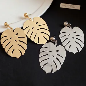 Primo piano di orecchini pendenti a foglia di monstera oro e argento su tessuto nero.