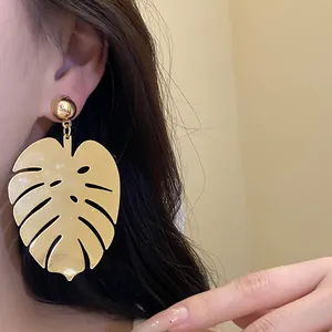 Primo piano dettagliato di orecchini a foglia di monstera dorata su una modella