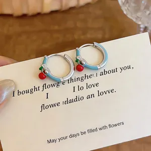Close-up of light blue enamel hoop earrings with small red cherry charms on card