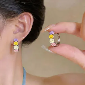 Detailed view of colorful enamel smiley face hoop earrings worn on a model's ear
