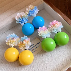 Close-up of colorful resin flower earrings with round beads in a beige jewelry display box.