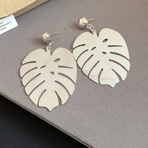 Primo piano di orecchini a foglia di monstera color argento con dettagli traforati su grigio