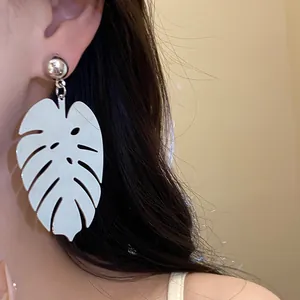 Primo piano di un orecchino pendente a forma di foglia di monstera in metallo argento indossato