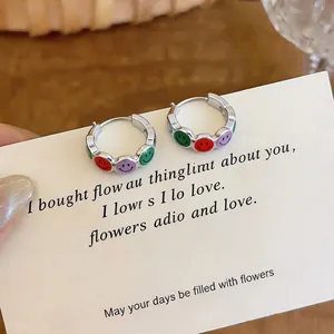 Close-up of silver-tone hoop earrings with colorful enamel smiley face charms