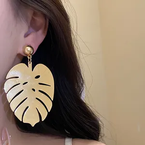Primo piano di un grande orecchino a forma di foglia di monstera dorata su una modella