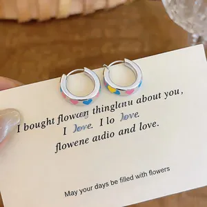 Close-up of geometric enamel hoop earrings with colorful heart patterns on display card