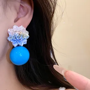 Close-up of resin flower earrings with a large bright blue sphere on an Asian model.