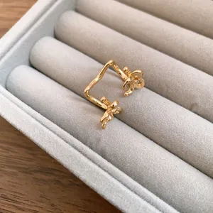 Detailed close-up of a gold bow ear cuff jewelry piece in a grey velvet tray.