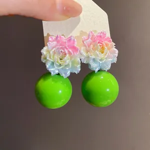 Close-up of resin flower stud earrings with glitter finish and vibrant green ball drops