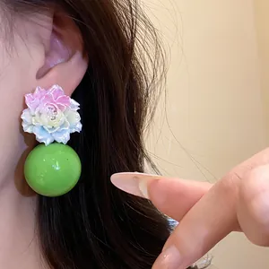 Detailed close-up of colorful resin flower earrings featuring a large vibrant green bead