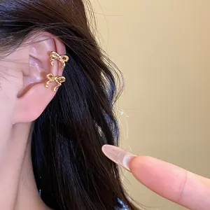Close-up of elegant gold bow-shaped ear cuffs worn on ear, niche luxury design.