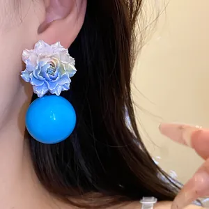 Detailed view of handmade resin flower earring with vibrant blue sphere worn on model's ear.