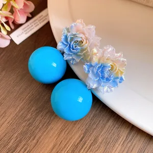 Detailed view of iridescent resin flower earrings with bright blue spherical studs