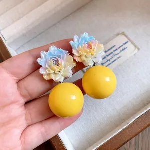 Close-up of resin flower earrings with large yellow beads and silver needles