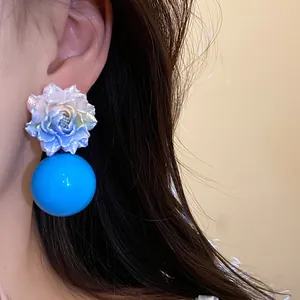 Close-up detail of sweet resort style resin flower earrings with a vibrant blue spherical drop
