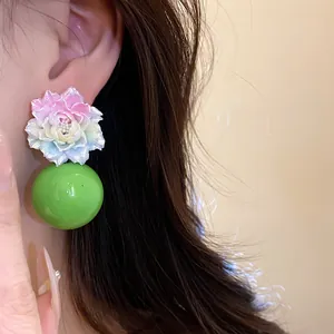 Close-up of resin flower earrings with gradient petals and a vibrant green round bead