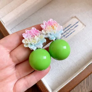 Macro view showing detailed resin flower design and bright green spherical drop earrings.