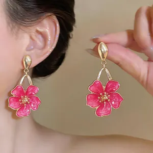 Detailed view of sweet pink enamel flower pendant earrings with gold-tone accents on ear