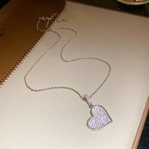Close-up detail of a sparkling zircon paved heart pendant necklace on a beige notebook