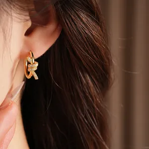 Macro detail showing the texture of 14k gold plated zircon knotted huggie earring on ear
