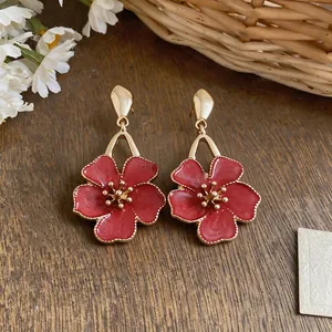 Detailed view of red enamel flower drop earrings presented on a rustic wooden background