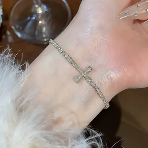 Detail of a sparkling 18k gold plated zircon cross bracelet worn on a female wrist.