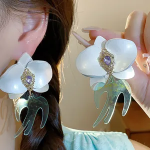 Détail macro de boucles d'oreilles élégantes avec fleurs en résine et hirondelles.