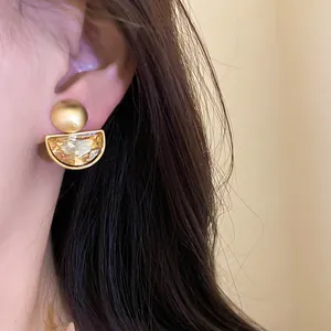 Close-up of vintage gold-toned earring with amber rhinestone in a semi-circular design