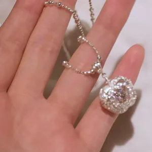 Close-up detail of a sparkling silver zircon apple heart pendant necklace on hand.