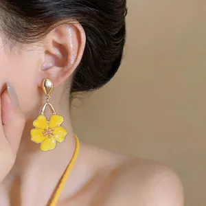 Detailed close-up view of vibrant yellow oil-drop flower dangle earrings on an Asian model