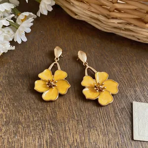 Close-up of yellow enamel flower drop earrings on a rustic wooden background